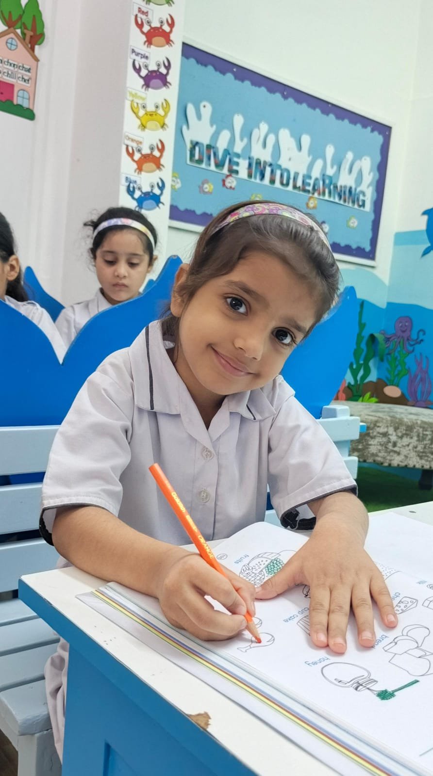 A Warsis student colouring with an orange pencil at her desk