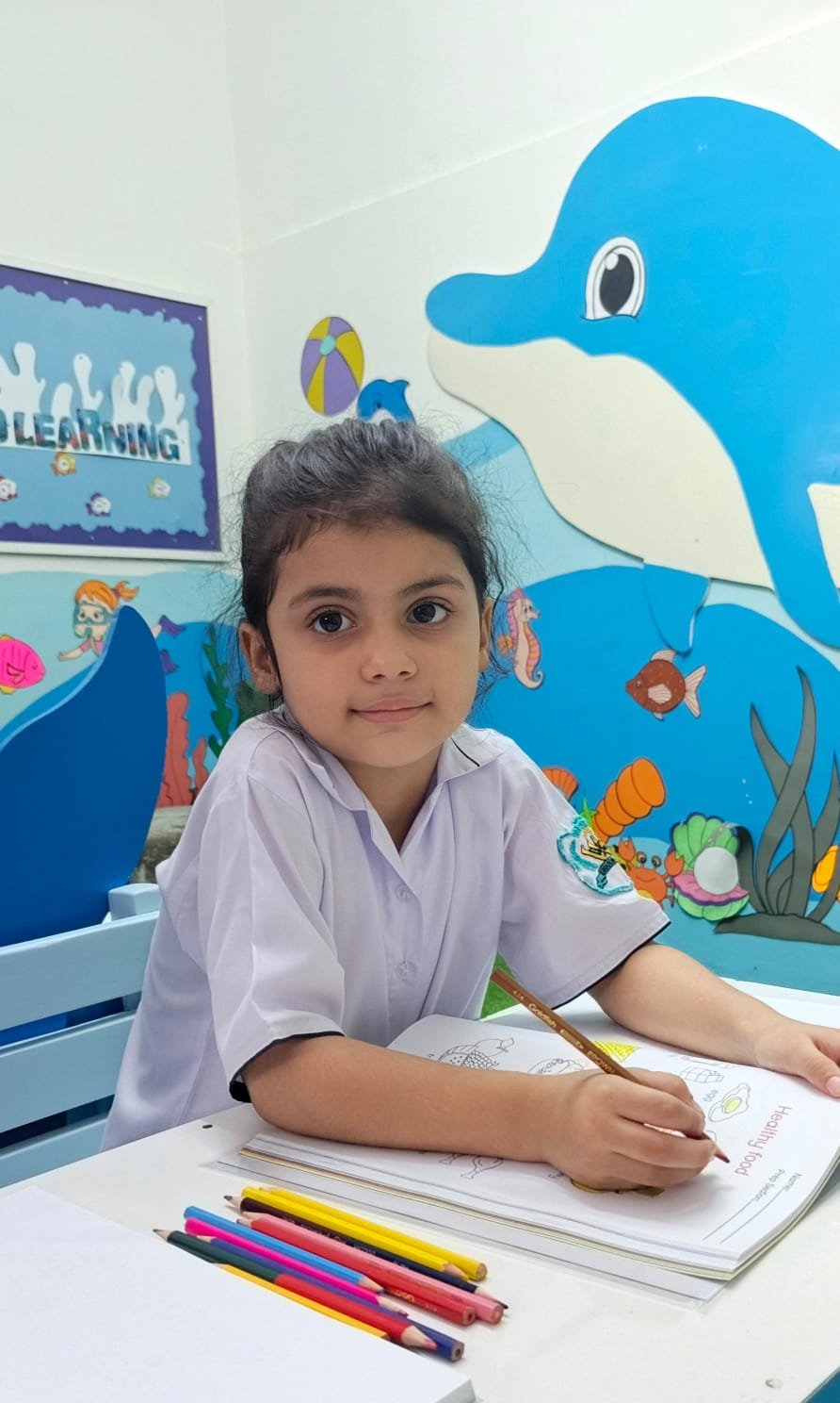 A Warsis student writing carefully in her workbook by the classroom mural