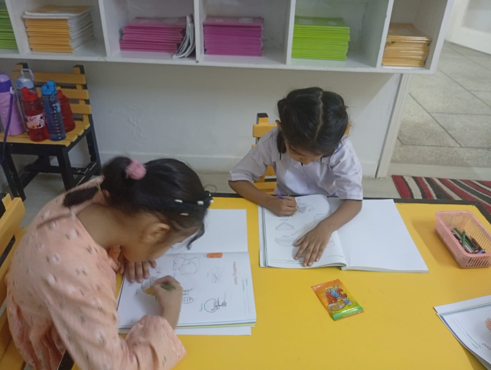 Two Warsis students colouring a worksheet together at a classroom table