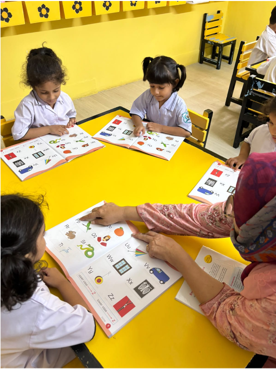 A Warsis teacher pointing out letters on a phonics chart with her students