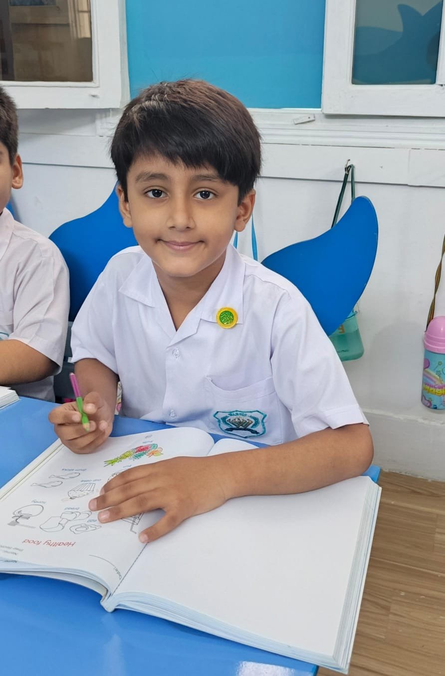 A Warsis student smiling over his open workbook